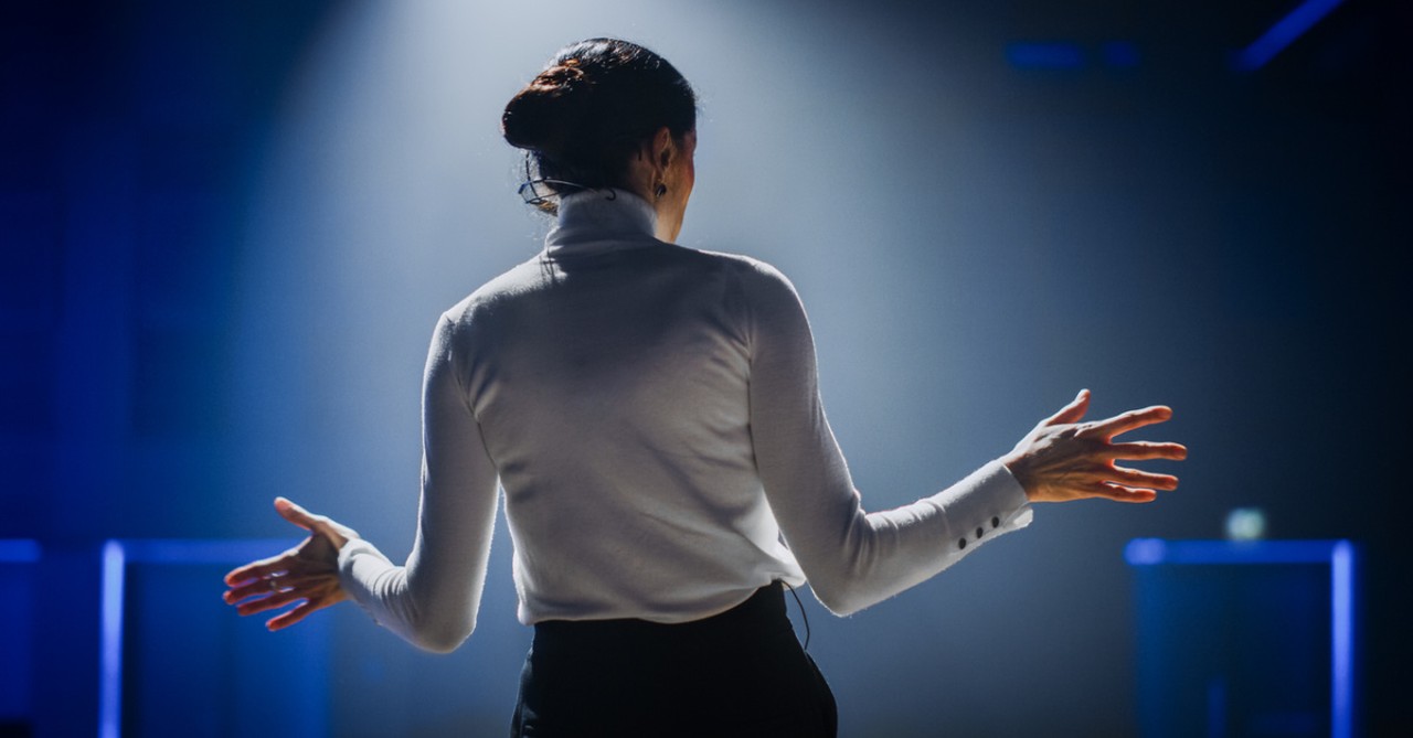 Woman speaking on stage, Saddleback stands behind female pastors