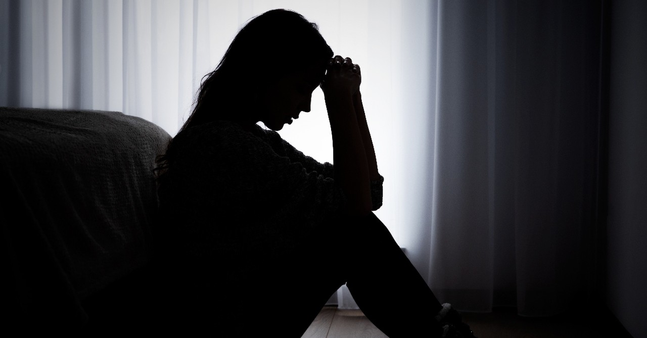 Woman sitting silhouetted looking depressed