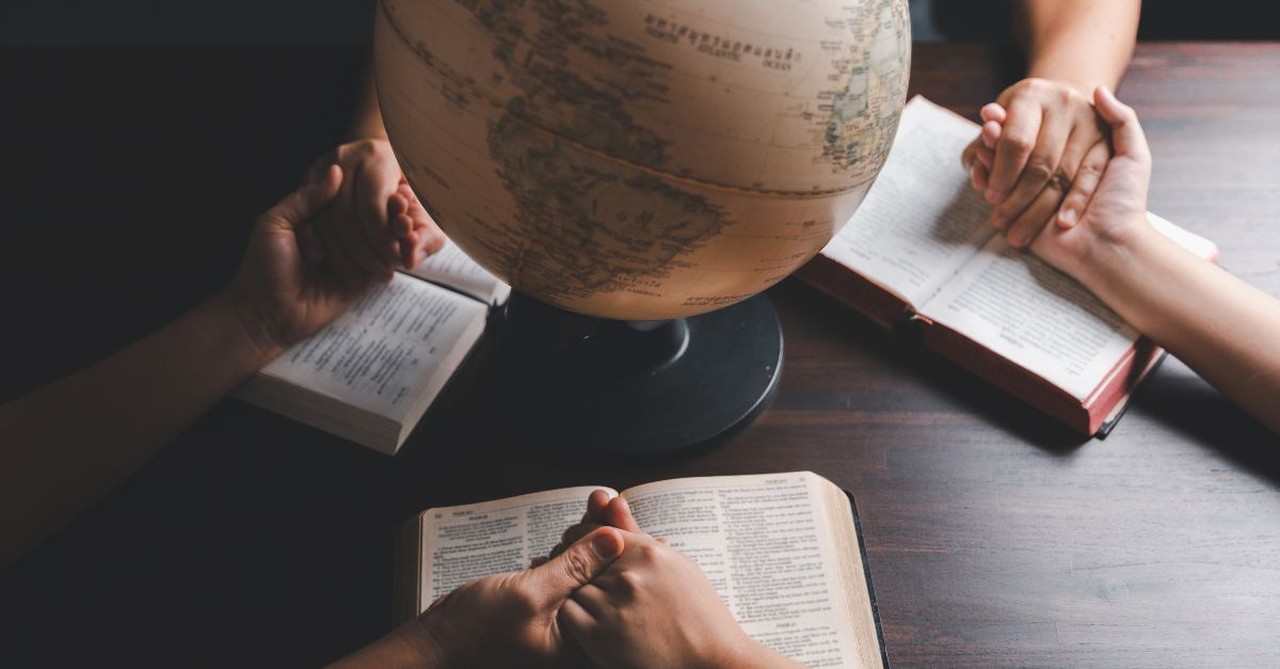 Hands held together over Bibles around the globe. Praying for the countries of the world.