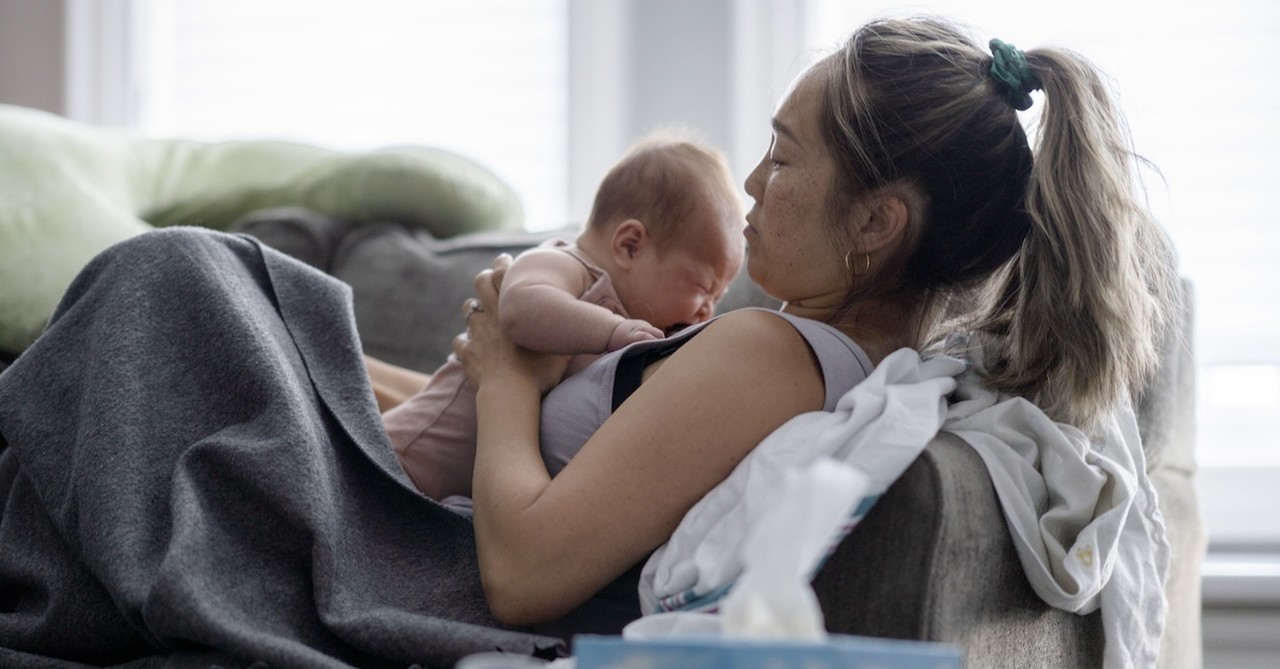 tired exhausted mom with newborn baby on couch postpartum