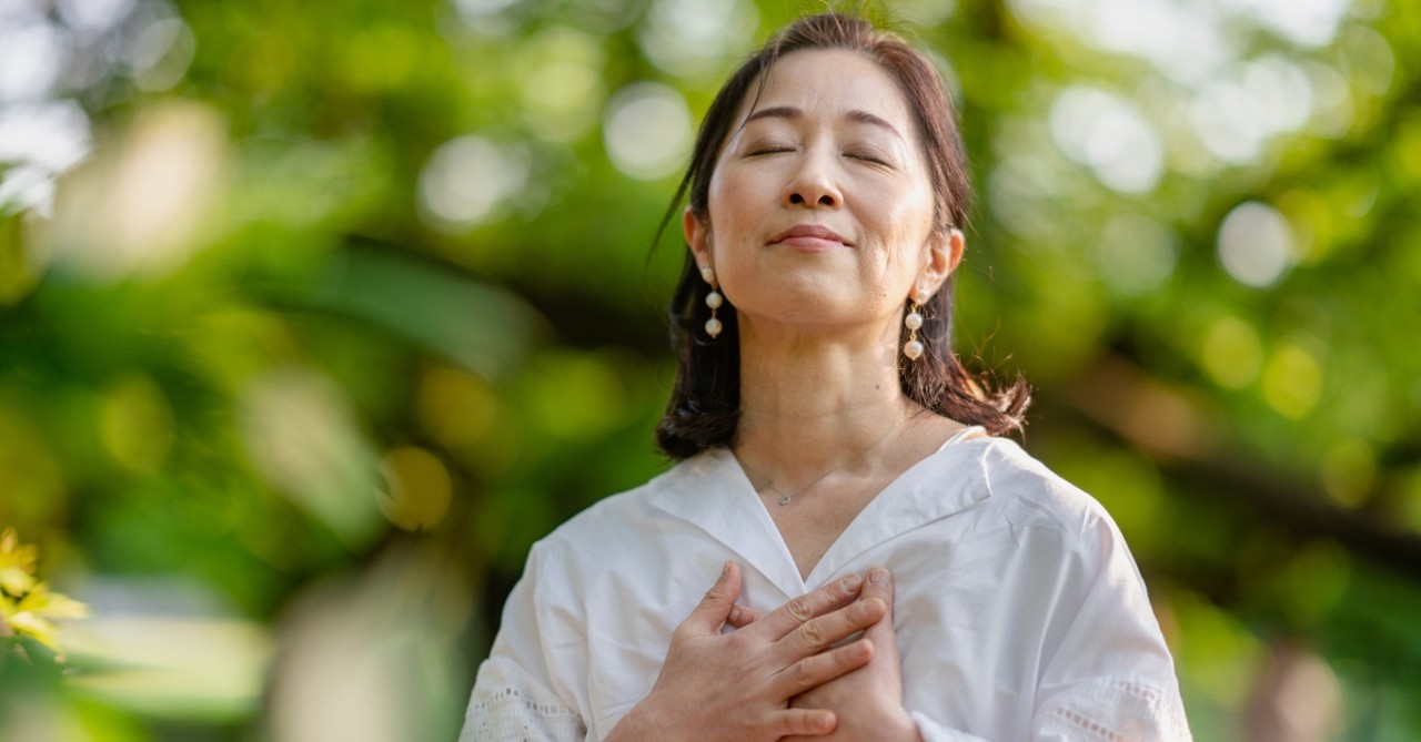 Peaceful older woman outside with her hands over her heart, praying or meditating