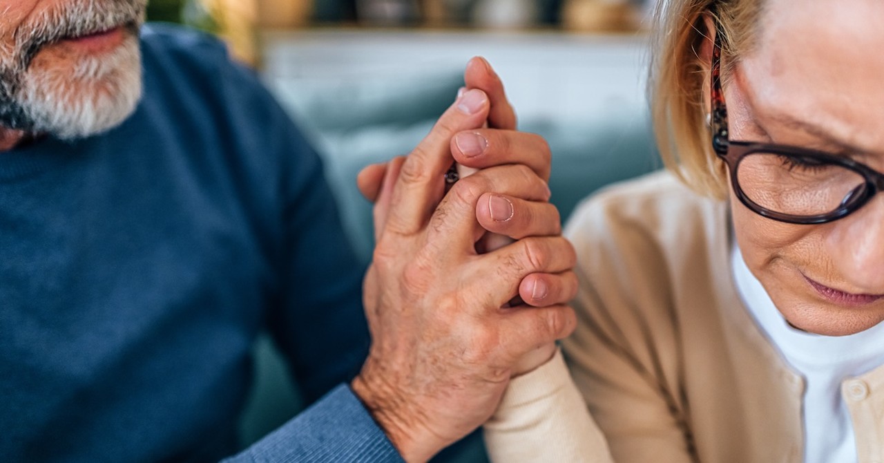 Stressed couple husband comforting wife on couch holding hands