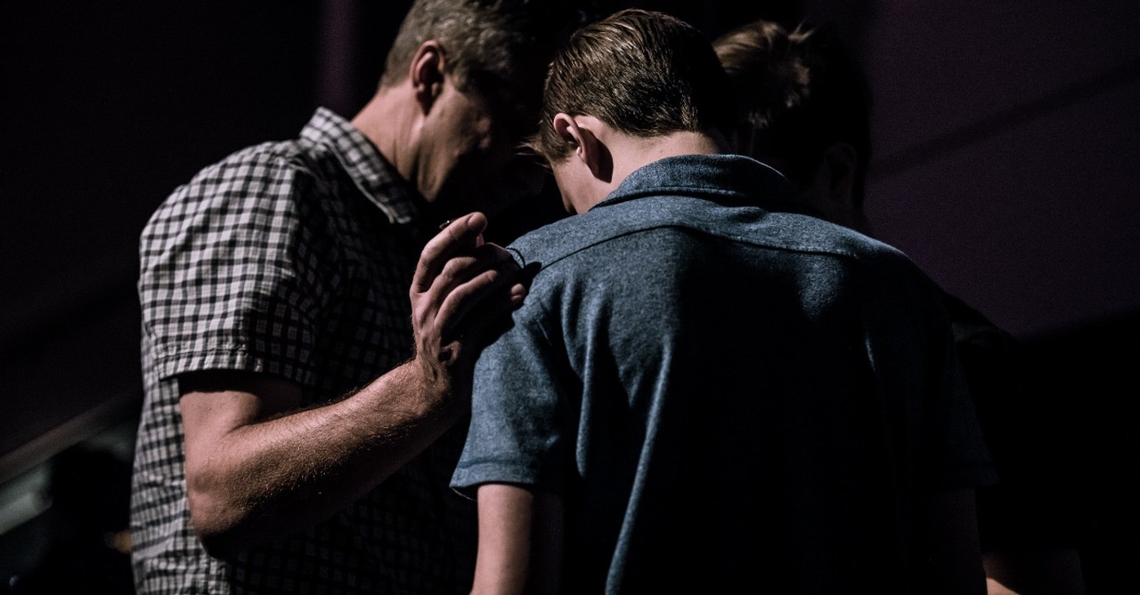Older church members praying over a younger man